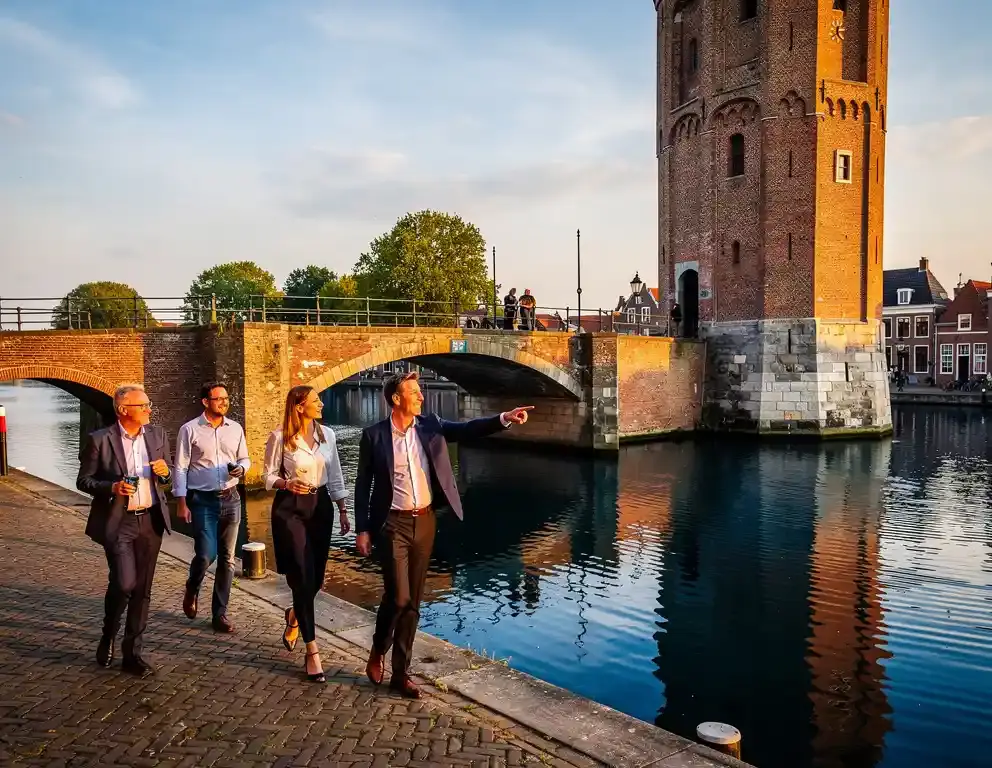 Collega's bij de middeleeuwse Hanzekade van Zutphen, met een historische ophaalbrug en bakstenen toren weerspiegeld in het IJsselkanaal.