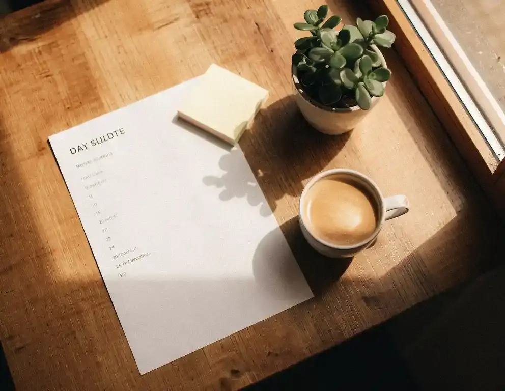 Dagplanning, koffie en sticky notes op een houten cafétafel met warm natuurlijk licht en terracotta tinten.