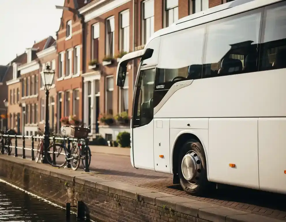 Moderne touringcar geparkeerd langs een rustige Amsterdamse gracht, bakstenen gevels en fietsen op de achtergrond in warm middaglicht.